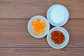 Sugar, chili powder and cooking vinegar with yellow chili. Flavoring ingredients in small white plates on wooden table.