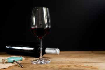 Red wine bottle lying down, red wine glass and old corkscrew