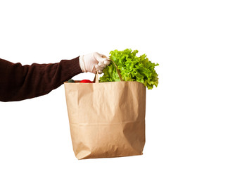 .A volunteer delivers food to those in need. Delivery donation. Green salad, red tomatoes, cucumbers in an eco-friendly paper bag. Hands in gloves. Isolate on a white background. Vegetables in a bag.