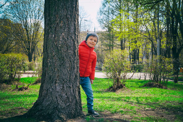 Naklejka na ściany i meble A boy in a red jacket is engaged in a sports field in the Park in the spring, climbing up the stairs. Swedish wall. Trips, sports classes for children, physical education, games in the fresh air.