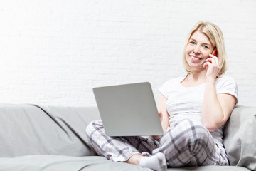 Smiling blonde woman is sitting on the couch and working online. Remote work during the coronavirus...