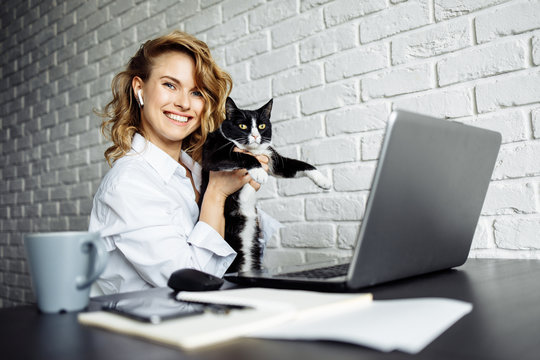 Happy woman with black cat in her arms sitting at table with laptop.