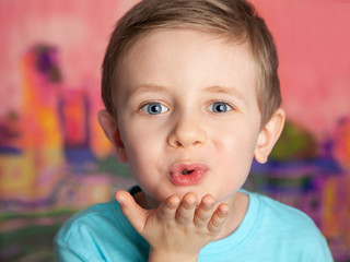 Portrait of a European blue-eyed boy blowing a kiss on a bright pink background. The child looks with a sly smile. Little ladies ' man.