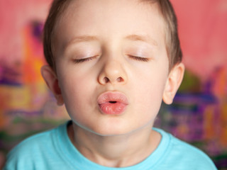 Portrait of a kissing boy. A European child sends the viewer a kiss with closed eyes on a bright pink background.