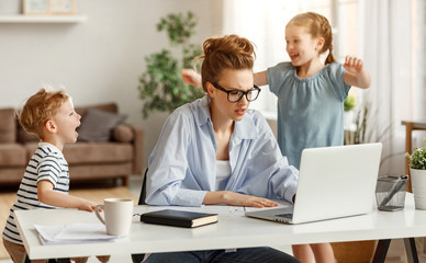 Little children distracting dedicated young woman working on laptop at home.