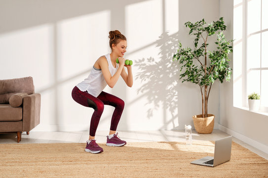 Young woman squatting with dumbbells at home.