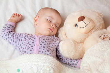 A beautiful baby girl is sleeping in a crib with a polar bear on a light background. Products for babies, sleep and rest.