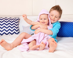 Brother and younger sister hug on the bed after bathing. Children's laughter, joy. The love of family.