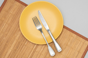 A yellow plate with a fork and knife on a Mat on a gray background. Top view with space for text