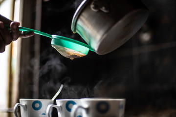 Tea being strained and poured into the cups from an aluminium tea pot in an Indian kitchen. Indian drink and beverages.