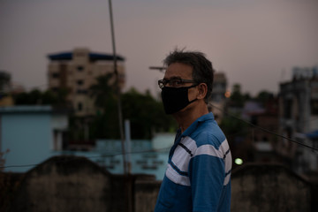 Portrait of an Indian old man wearing corona preventive mask on a rooftop during sunset in home isolation in green background.Indian lifestyle, disease and home quarantine.