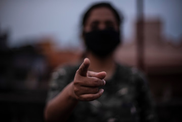 Blurred portrait of an Indian young woman with corona preventive mask pointing her finger on a rooftop in an afternoon in home isolation.Indian lifestyle, disease and home quarantine.