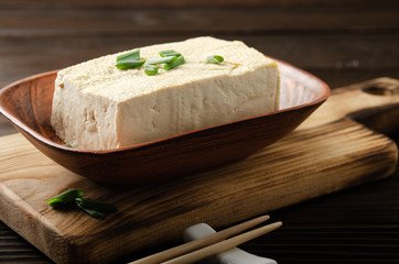 Soybean tofu vegetable bean curd in clay bowl on kitchen table with chives and chopsticks aside