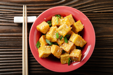 Flat lay view at crispy deep stir fried tofu cubes with chives in clay dish on wooden kitchen table