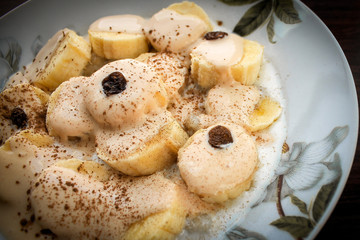 Banana fruit dessert with melted ice cream with chocolate, raisins and cinnamon and cocoa. Dark background.