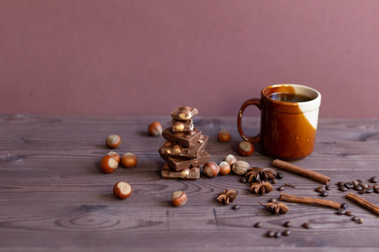 Pieces of dark chocolate with nazel nuts, cup of coffee, spices on brown wooden backgrouns