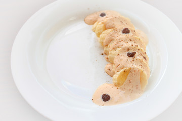 Banana fruit dessert with melted creme brulee ice cream, raisins and cinnamon on a white plate. White background. Insulation