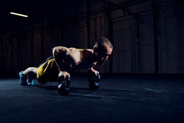 Athletic man exercising kettlebell push-ups at gym