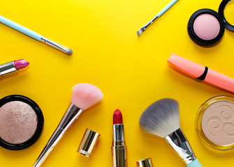 Beautiful makeup: pink lipstick, blush, powder, cosmetic brushes on a bright yellow background
