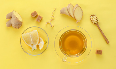 Ginger tea with lemon and spices in glass Cup with spoon and sugar on yellow paper background, top view