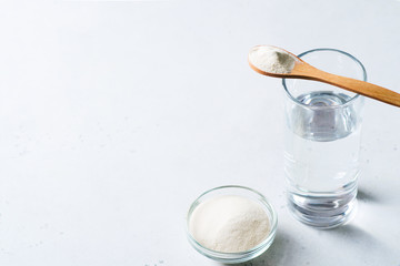 Collagen powder in spoon on glass of water, supplement, healthy and anti age concept flat lay on white background