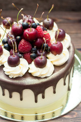 Homemade cake with melted chocolate decorated with whipped cream and fresh cheries on top. Rustic wooden background.