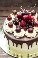 Homemade cake with melted chocolate decorated with whipped cream and fresh cheries on top. Rustic wooden background.