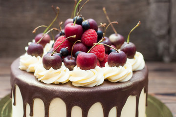 Homemade cake with melted chocolate decorated with whipped cream and fresh cheries on top. Rustic wooden background.
