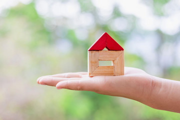Small toy wooden house in hands with green nature background