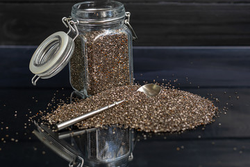 Black chia seeds in glassware contain healthy vitamins and minerals. On a black background with a metal spoon.