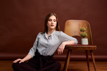 Gorgeous young female in classic suit, black shoes and grey coat. Vintage chair. Woman's clothes.