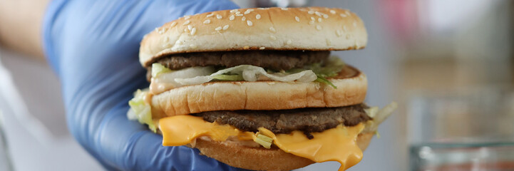 Close-up of persons hand holding tasty burger in protective blue gloves with precise accuracy. Investigation under high-tech microscope. Health study and laboratory concept