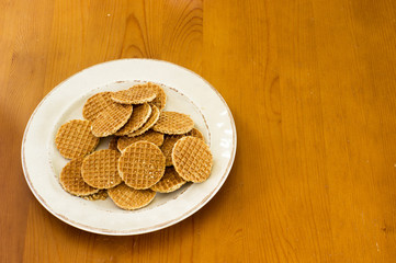 Plate of mini stroopwafels on a wooden table. A stroopwafel is a traditional dutch cookie made from two thin layers of baked dough joined by a caramel filling