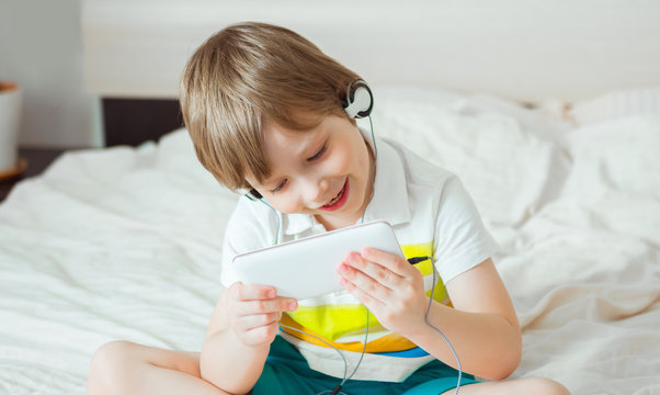 Modern little child sitting on bed with smartphone in his hands