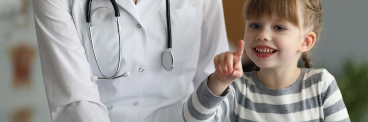Close-up of smiling child pointing finger and holding paper folder. Happy kid looking at camera with gladness and smiling. Healthcare and prevention concept