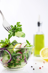 Vegan concept, vegetable salad in a transparent glass plate, in a blurred background olive oil in a bottle, fork over a plate with salad, shallow depth of field, selective focus.