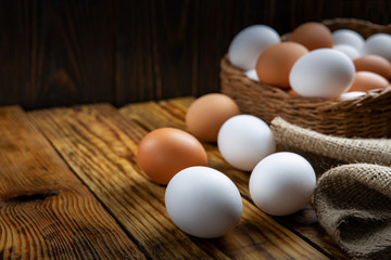 Farm eggs white and brown lie on a wooden table and in a basket, close-up, low light, selective focus, shallow depth of field. Organic food concept