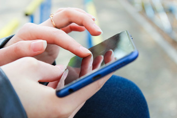 The girl is holding a smartphone on which she is typing a message or comment. Communication in social networks.