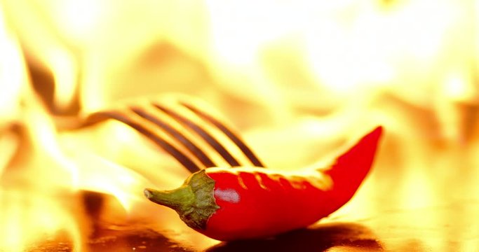 Red chili pepper on a fork burns in a bright flame of fire.