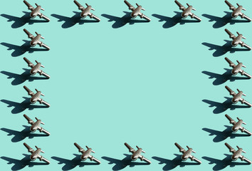 Frame of eigteen metal figures of small airplanes with shadows with the same space between them on the light mint color background. Conceptual geometric art trendy aviation boarder with empty space