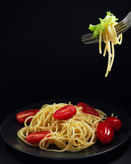 Concept a black plate with spaghetti and cherry tomatoes and a fork with a bunch of pasta. Black background with space for text