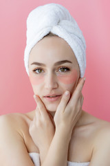 Studio shot of satisfied caucasian freckled woman wearing white towel on head, with collagen patches under eyes, standing naked against pink background. Skin care, cosmetic product concept