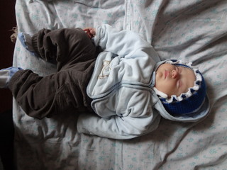 Sleeping little boy in a blue cap with a white frill. Close-up. A child in a blue blouse lies in bed with his eyes closed. Newborn snub-nosed baby with chubby cheeks.