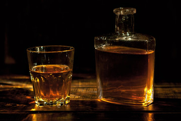 A glass of alcohol near a bottle. Old whiskey bottle on black wooden table. Drinks on a dark...