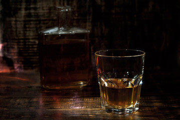 A glass of alcohol near a bottle. Old whiskey bottle on black wooden table. Drinks on a dark blurred background.