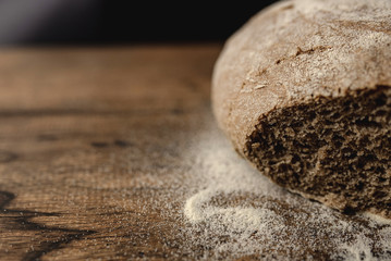 Close up of loaf of rye black sliced bread on wooden table with flour. Dark background with free space for text on the left.