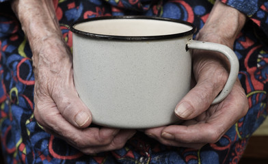 In her hands, an old grandmother of 90 years holds in her hand a metal mug with water, poverty and...