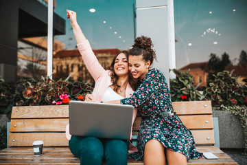 Two excited female friends celebrating success reading good unexpected news, great offer  in a...