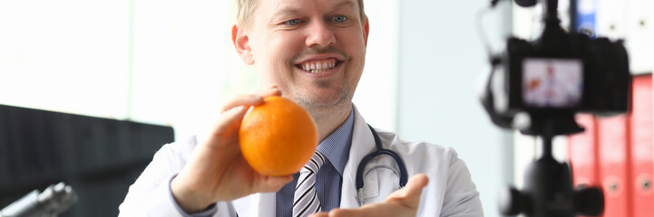 Nutritionist doctor speaks about benefits orange. Young doctor tells in fascinating way allergies and nutrition. Author reveals relevant topics related to health and shares professional advice
