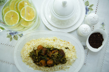 A bowl of white ceramic salt and pepper. Shah pilaf. Khan pilaf in a pita. Black pepper in a white ceramic pot . There is meat and plum chestnuts on the pilaf . Rice in a white plate. Sliced lemon .